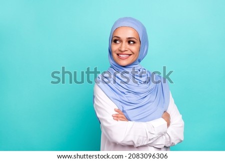 Photo of confident dreamy young lady dressed islamic hijab smiling arms crossed looking empty space isolated teal color background