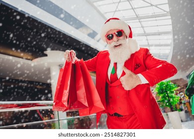 Photo of confident pretty santa claus wear dark glasses holding bargains showing thumb up indoors shopping center - Powered by Shutterstock