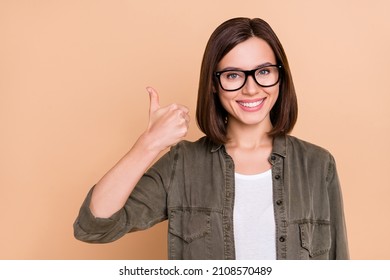 Photo of confident promoter lady raise thumb up positive feedback wear specs khaki shirt isolated beige color background - Powered by Shutterstock