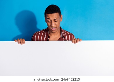 Photo of confused guy wear striped stylish shirt over white t-shirt look at white placard empty space isolated on blue color background - Powered by Shutterstock