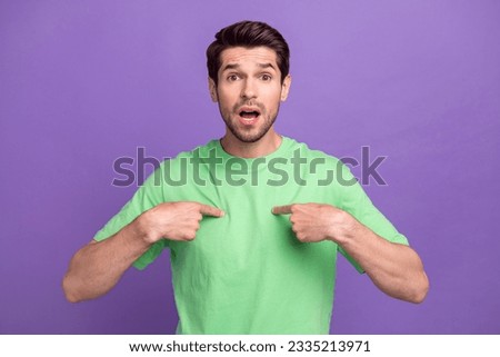 Photo of confused offended man with stubble dressed green t-shirt astonished indicating at himself isolated on purple color background