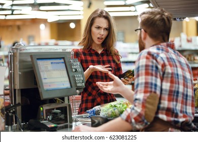 Photo of confused young lady standing in supermarket shop near cashier's desk. Looking aside.