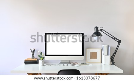 Photo of Contemporary Workspace.
White blank screen monitor on modern working desk. Equipment on table. Modern office concept. 