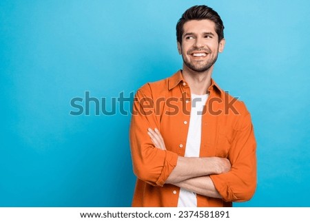 Photo of cool dreamy guy wear orange shirt smiling arms crossed looking empty space isolated blue color background