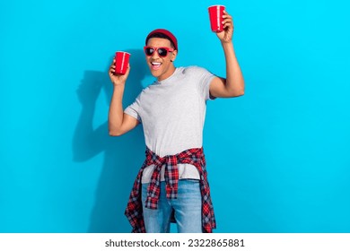 Photo of cool funny man wear grey t-shirt dark glasses drinking beer having fun isolated blue color background
