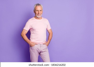 Photo Of Cool Old Man Hands Pockets Beaming Smile Look Camera Wear Pink T-shirt Pants Isolated Violet Color Background