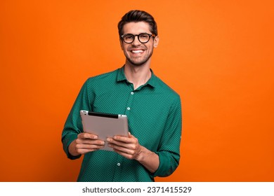 Foto de un tipo positivo genial que usa camisa verde que comunica el moderno gadget aislado color naranja fondo