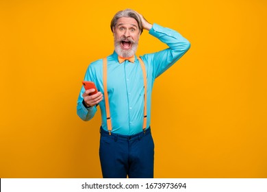 Photo Of Cool Shocked Grandpa Hold Telephone Open Mouth Surprised New Model Smart Phone Wear Blue Shirt Suspenders Bow Tie Pants Isolated Yellow Color Background