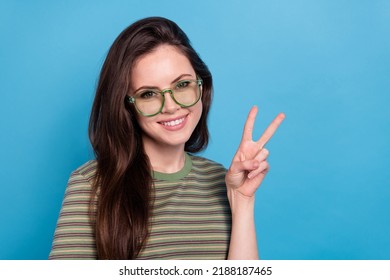 Photo of cool young brunette lady show v-sign wear eyewear green t-shirt isolated on blue background - Shutterstock ID 2188187465