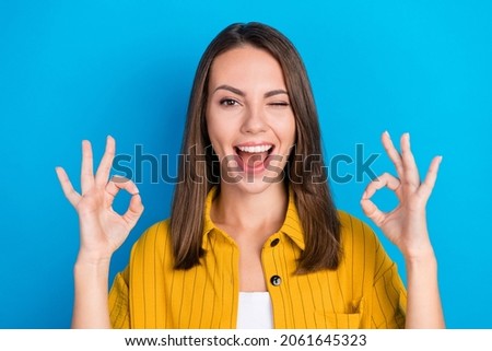 Photo of cool young brunette lady show okey blink wear yellow shirt isolated on blue color background