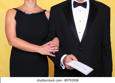 Photo of a couple in black tie evening wear, the man is holding an invitation.