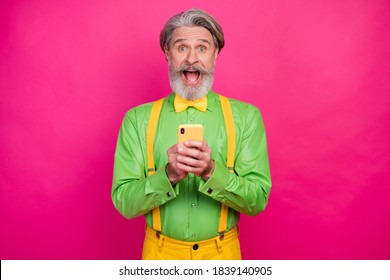 Photo Of Crazy Amazed White Haired Grandpa Hold Telephone Read Blog Post Comments Wear Green Shirt Yellow Suspenders Bow Tie Pants Isolated Bright Pink Color Background