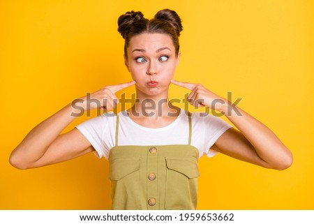 Photo of crazy girl crossed eyes press fingers puffed cheeks wear green overall isolated yellow background