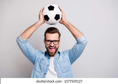 Photo Of Crazy Handsome Guy Raising White Black Soccer Ball Above Head Yell Support Team Football Match Wear Specs Casual Denim Outfit Isolated Grey Color Background