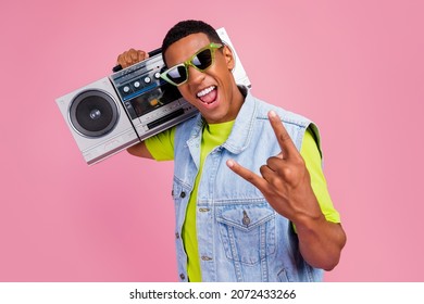 Photo of crazy millennial brunet guy hold boom box yell show rock sign wear eyewear t-shirt vest jeans isolated over pink color background