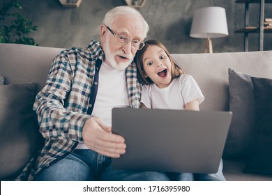 Photo Of Crazy Old Aged Grandpa Pretty Small Granddaughter Sit Sofa Stay House Quarantine Watch Comedy Humorous Movie Notebook Good Mood Modern Design Interior Living Room Indoors