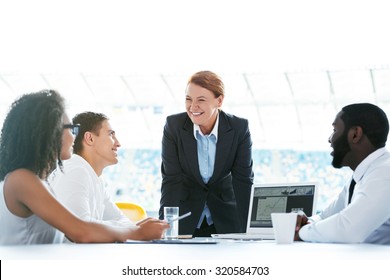 Photo Of Creative Multi Ethnic Business Group. Mixed Race Business Team Using Laptop And Discussing Project. Accent On Leader Of Group. White Modern Office Interior With Big Window