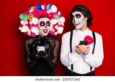 Photo Of Creepy Couple Man Lady Hold Telephones Read Dark Humor Jokes Share Funny Posts Wear Black Dress Death Costume Sugar Skull Roses Headband Suspenders Isolated Red Color Background