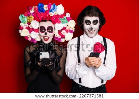 Photo of creepy zombie two people man lady hold telephones excited find online shop immortality potion wear black dress death costume roses headband suspenders isolated red color background