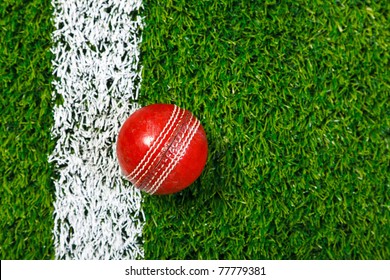 Photo of a cricket ball on a grass next to the white line, shot from above.