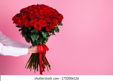 Photo of cropped man arms hold big one hundred red bright roses bunch giving girlfriend surprise hiding face secret admirer arrangement delivery concept isolated over pink color background