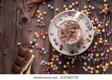 photo cup of coffee, topped with cocoa powder. The cup is on a saucer, surrounded by colorful candy-coated chocolates. There are also pieces of chocolate bars - Powered by Shutterstock