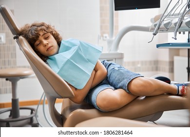 Photo Of A Curly Brunette Child Wearing A Sanitary Bib Napping Peacefully In A Chair In Dentist Lab