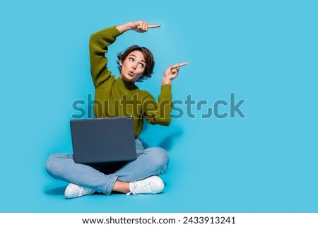 Photo of cute adorable girl sit floor wear trendy clothes arms above head look empty space isolated on cyan color background