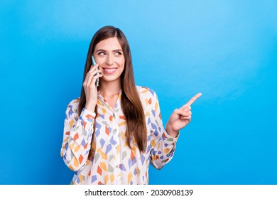 Photo of cute adorable young lady wear print shirt smiling talking modern device pointing empty space isolated blue color background - Shutterstock ID 2030908139