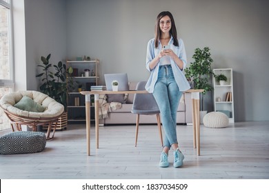 Photo of cute business lady hold cellphone look camera wear spectacles jeans sneakers shirt in home office indoors