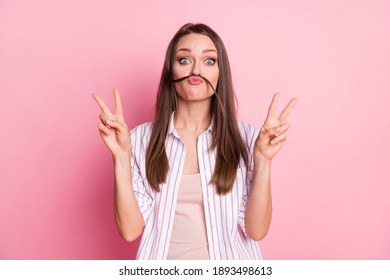 Photo of cute carefree young woman dressed casual white clothes made hair mustaches showing v-sign isolated pink color background