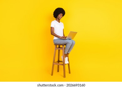 Photo of cute charming dark skin lady wear t-shirt sitting bar chair typing modern device smiling isolated yellow color background