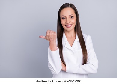 Photo of cute charming woman doc dressed white coat pointing thumb up empty space smiling isolated grey color background