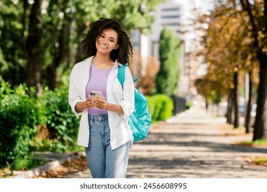 Photo of cute dreamy woman dressed white shirt backpack chatting modern device walking university outdoors urban city park - Powered by Shutterstock