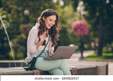 Photo Of Cute Funny Brunette Lady Sit Near Fountain Laughing On Laptop Wear Green Pants Shirt Top Bag In Park Outdoors