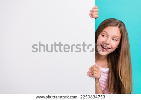 Photo of cute funny girl peeking look behind empty space blank isolated on teal color background