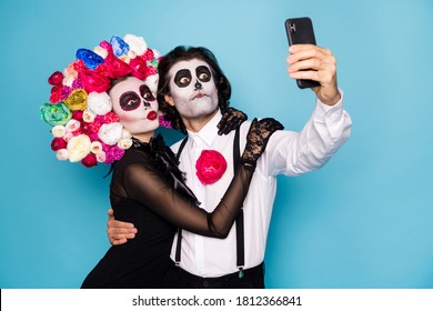 Photo of cute funny zombie couple man lady girl embrace hold telephone make selfie translate festival wear black dress death costume roses headband suspenders isolated blue color background