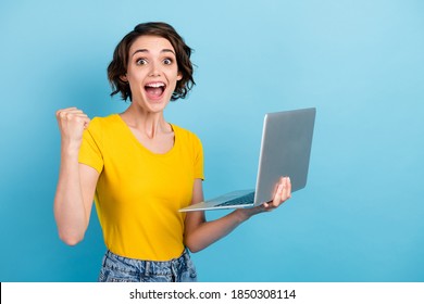 Photo of cute girl hold computer open mouth raise fist wear yellow t-shirt isolated blue color background - Shutterstock ID 1850308114