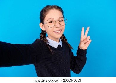 Photo of cute happy nice schoolgirl good mood make selfie show v-sign isolated on blue color background