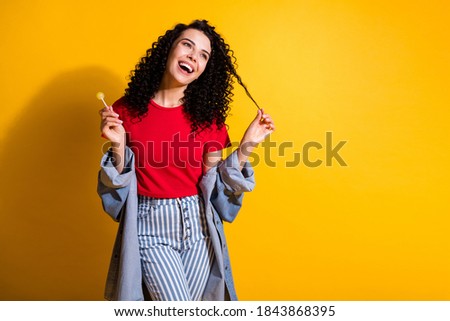 Photo of cute lady hold lollipop play curl look empty space wear red t-shirt striped jeans jacket isolated yellow color background