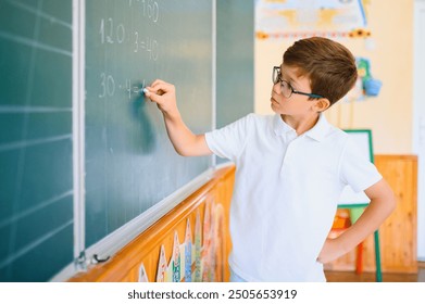 Photo of cute little schoolboy diligent write chalk solve math problem dressed stylish uniform classroom blackboard background - Powered by Shutterstock