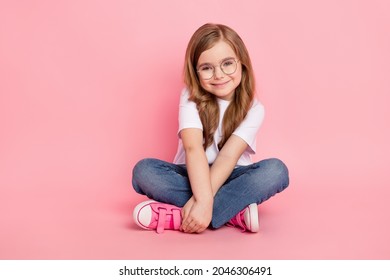 Photo of cute lovely small girl sit floor hands hold wear specs white t-shirt jeans shoes isolated pink color background - Powered by Shutterstock