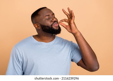 Photo of cute millennial brunet guy try food wear blue t-shirt isolated on beige color background - Shutterstock ID 2116239296
