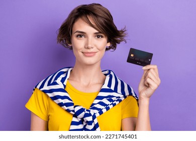 Photo of cute positive woman wear tied sweater showing credit card empty space isolated purple color background