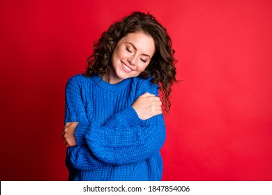 Photo of cute pretty dreamy lady curly hairstyle beaming white smile cuddle herself eyes closed fantasize wear blue knitted sweater pullover isolated red color background