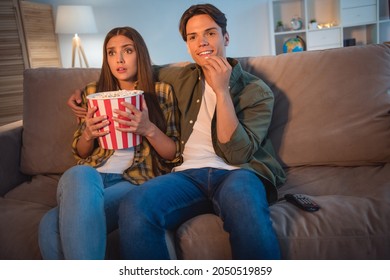 Photo Of Cute Scared Young Couple Wear Casual Shirts Smiling Sitting Couch Watching Scary Movie Eating Pop Corn Indoors House Room