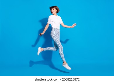 Photo of cute shiny young woman dressed casual clothes running looking back empty space smiling isolated blue color background