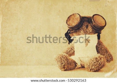 Photo of cute teddy bear with pilot glasses on wooden table. Sepia style and textured image