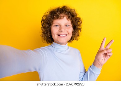 Photo Of Cute Teen Curly Hairdo Boy Do Selfie Show V-sign Wear Blue Turtleneck Isolated On Yellow Color Background