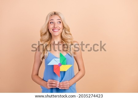Photo of cute thoughtful young lady wear blue singlet smiling holding windmill looking empty space isolated beige color background